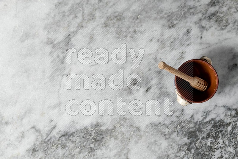 Decorative Pottery Pot with wooden honey handle in it, on grey marble flooring, Top View