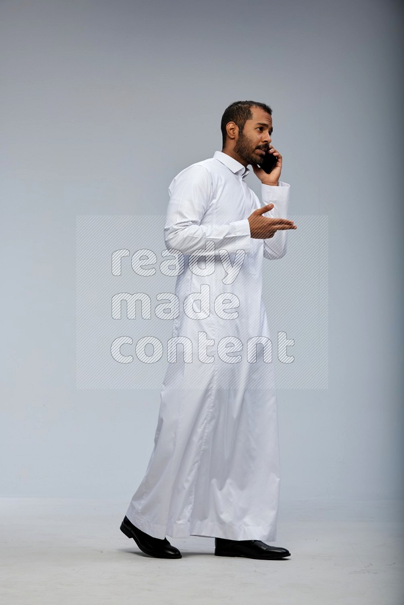 Saudi man wearing Thob standing talking on phone on Gray background