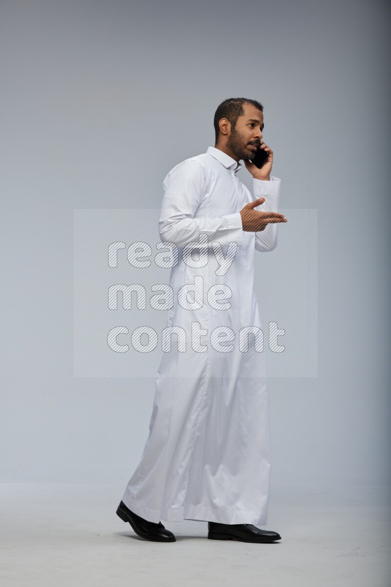 Saudi man wearing Thob standing talking on phone on Gray background