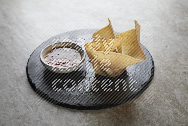wonton cups with soy sauce ramkin on circle slate on grey textured counter top