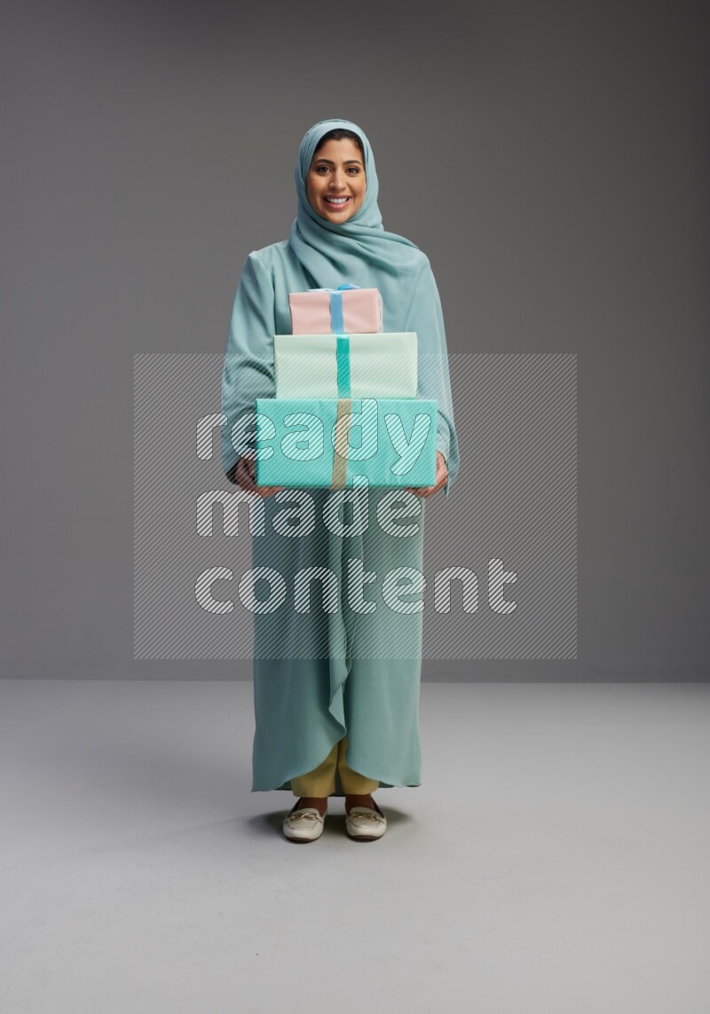 Saudi Woman wearing Abaya standing holding gift box on Gray background