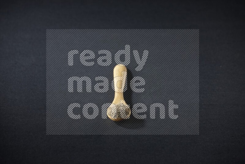 ملعقة خشبية ممتلئة ببودرة الهيل على خلفية سوداء