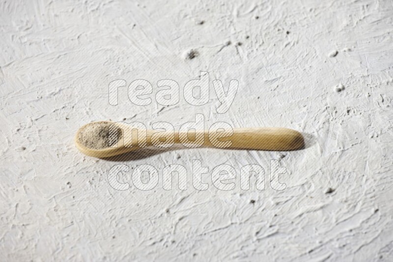 A wooden spoon full of white pepper powder on textured white flooring