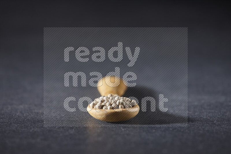 ملعقة خشبية مملوءة بحبات الفلفل الأبيض على أرضية سوداء