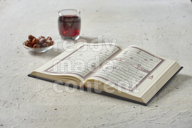 Quran with dates, prayer beads and different drinks all placed on textured white background