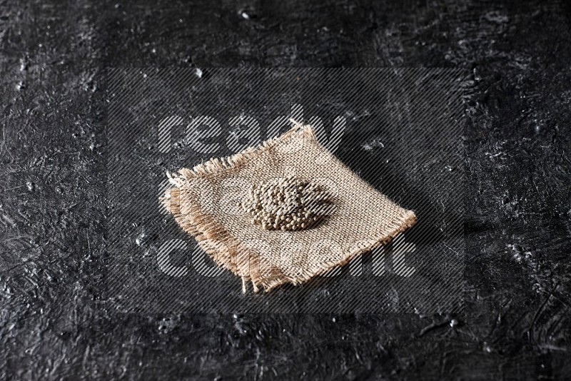 White pepper beads on a burlap piece of fabric on textured black flooring