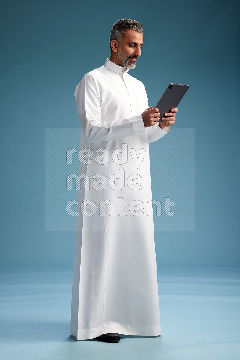 Saudi man waring thob with tablet on blue background