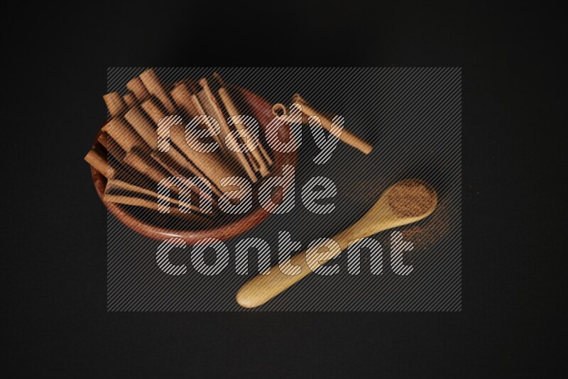 Cinnamon sticks in wooden bowl and cinnamon powder in a wooden spoon on black background