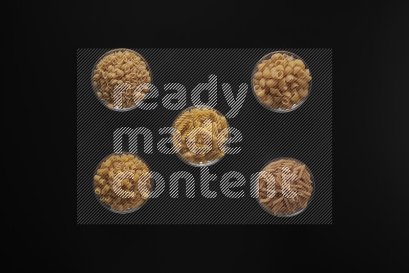 Different pasta types in 5 glass bowls on black background