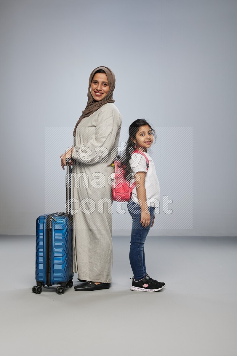 Mom and daughter standing pulling a carry-on bag on gray background