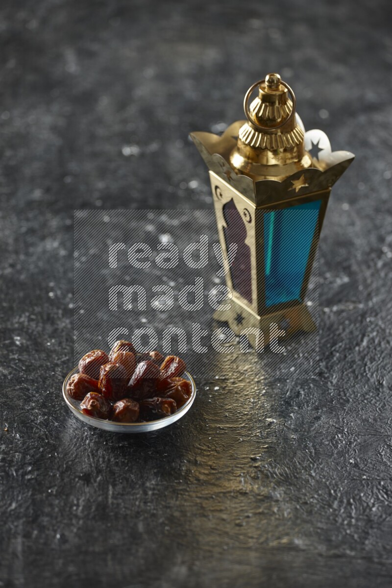 A golden lantern with different drinks, dates, nuts, prayer beads and quran on textured black background