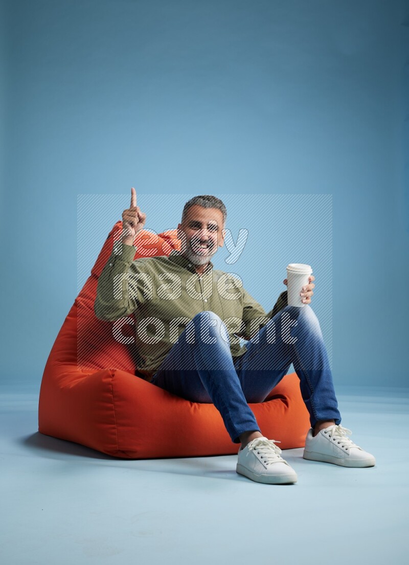 A man sitting on an orange beanbag and drinking coffee