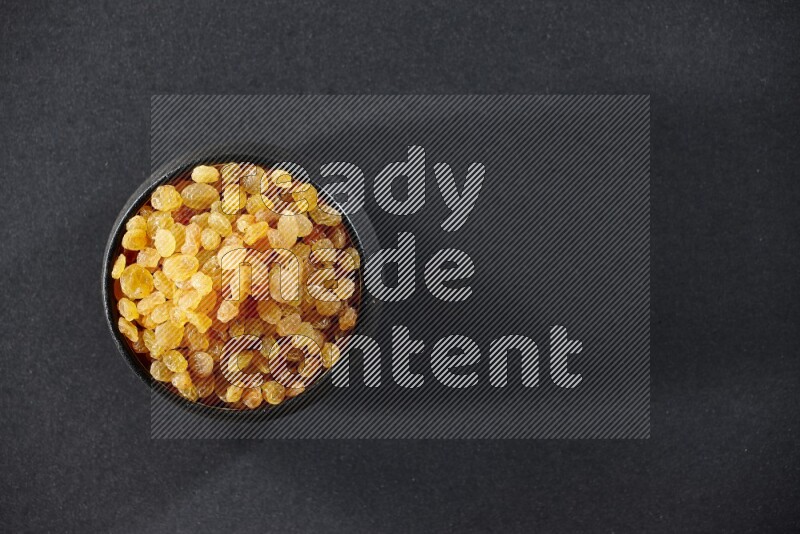 A black pottery bowl full of raisins on a black background in different angles