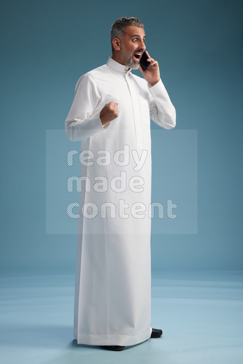 Saudi man wearing thob talking on the phone on blue background