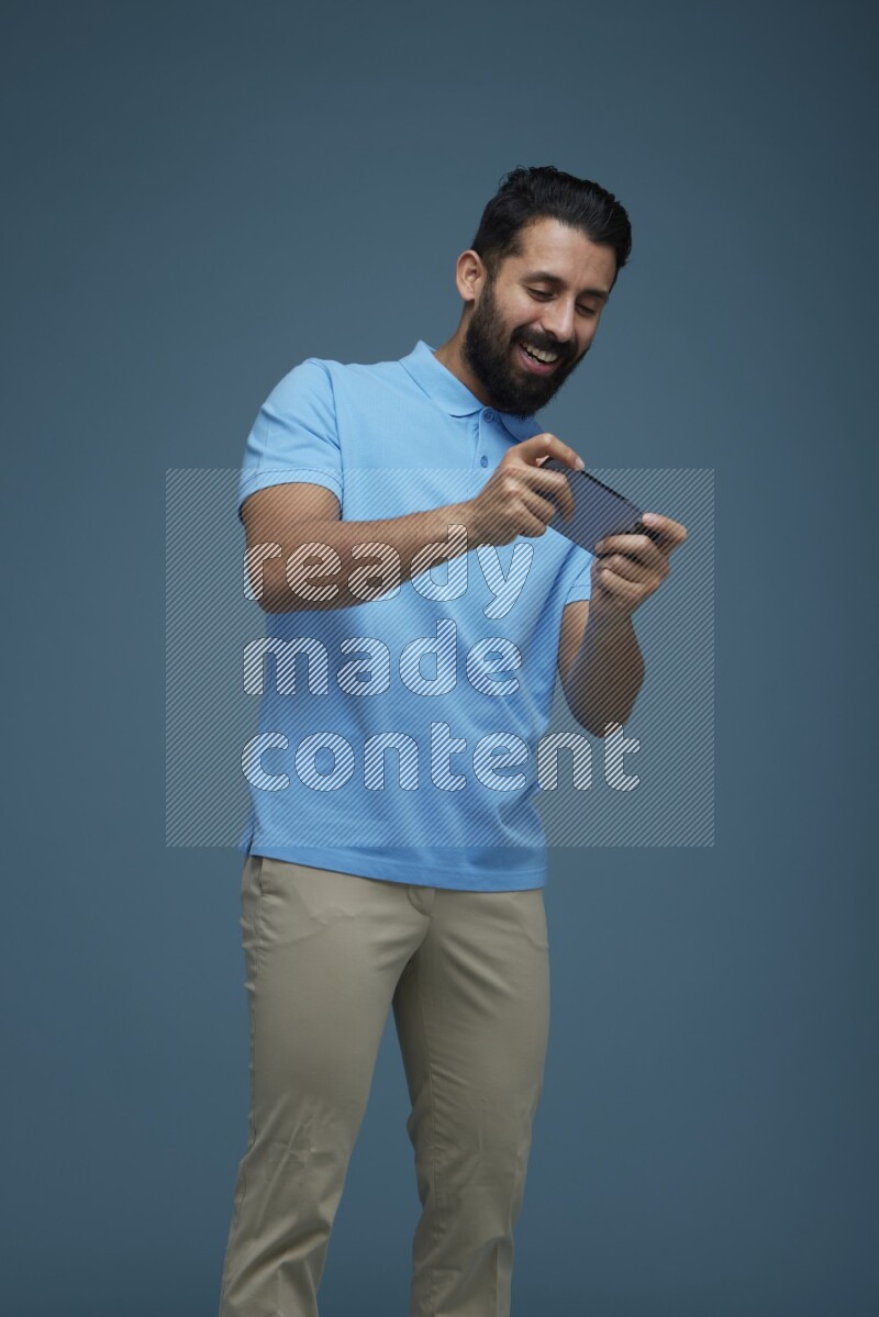 Man playing a game on his phone in a blue background wearing a Blue shirt