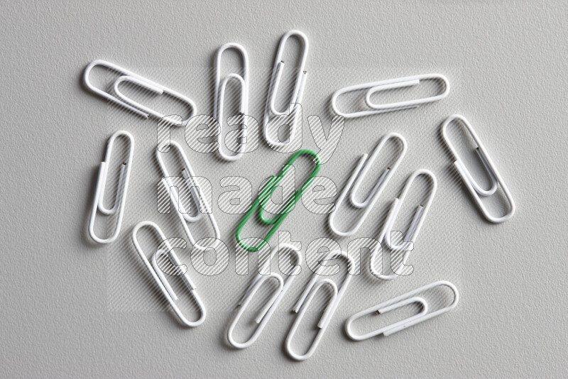 A green paperclip surrounded by bunch of white paperclips on grey background