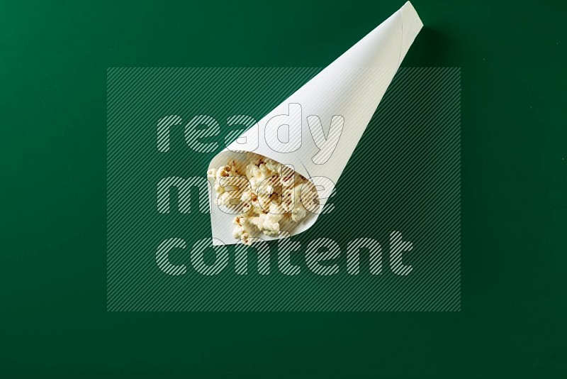 A paper cone full of popcorn on a green background in a top veiw shot