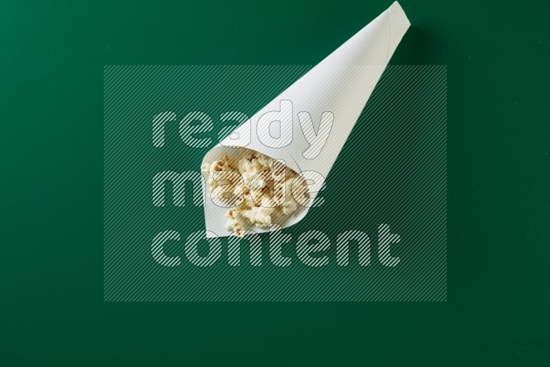 A paper cone full of popcorn on a green background in a top veiw shot