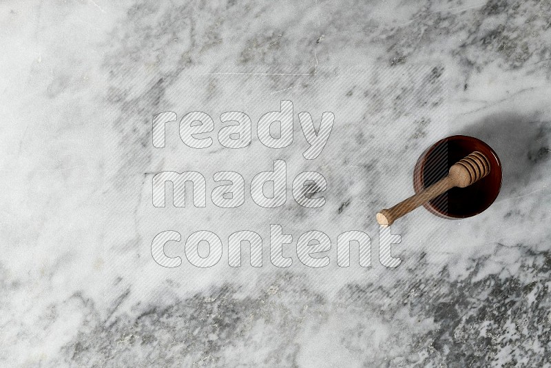 Brown Pottery Bowl with wooden honey handle in it, on grey marble flooring, Top View
