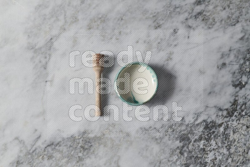 Multicolored pottery bowl with wooden honey dipper on the side on grey marble background