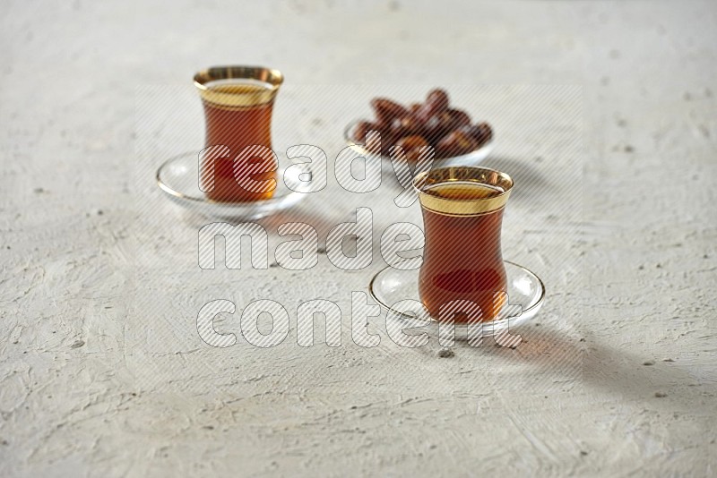 A tea glass cup with dates and coffee on textured white background