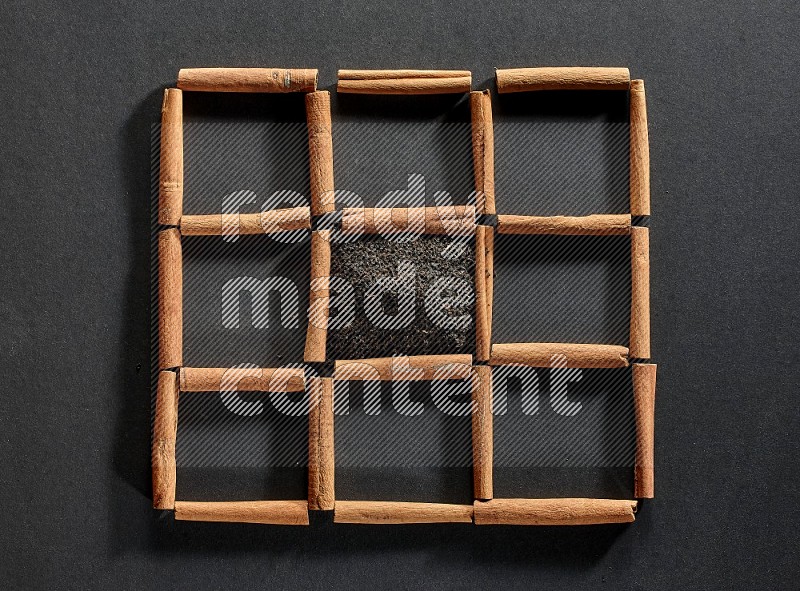 9 squares of cinnamon sticks full of tea in the middle surrounded by nutmeg, dried mint, cloves, dried basil, dried ginger, cinnamon, star anise and cardamom on black flooring