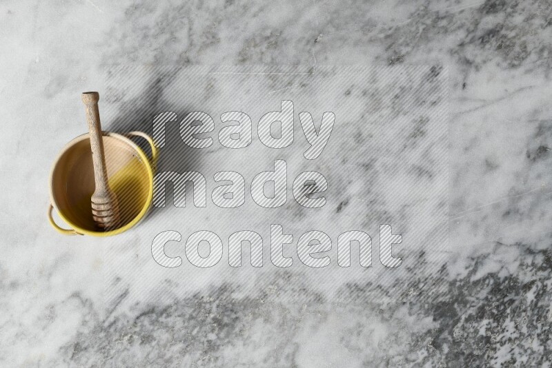 Multicolored pottery bowl with wooden honey dipper in it on grey marble background