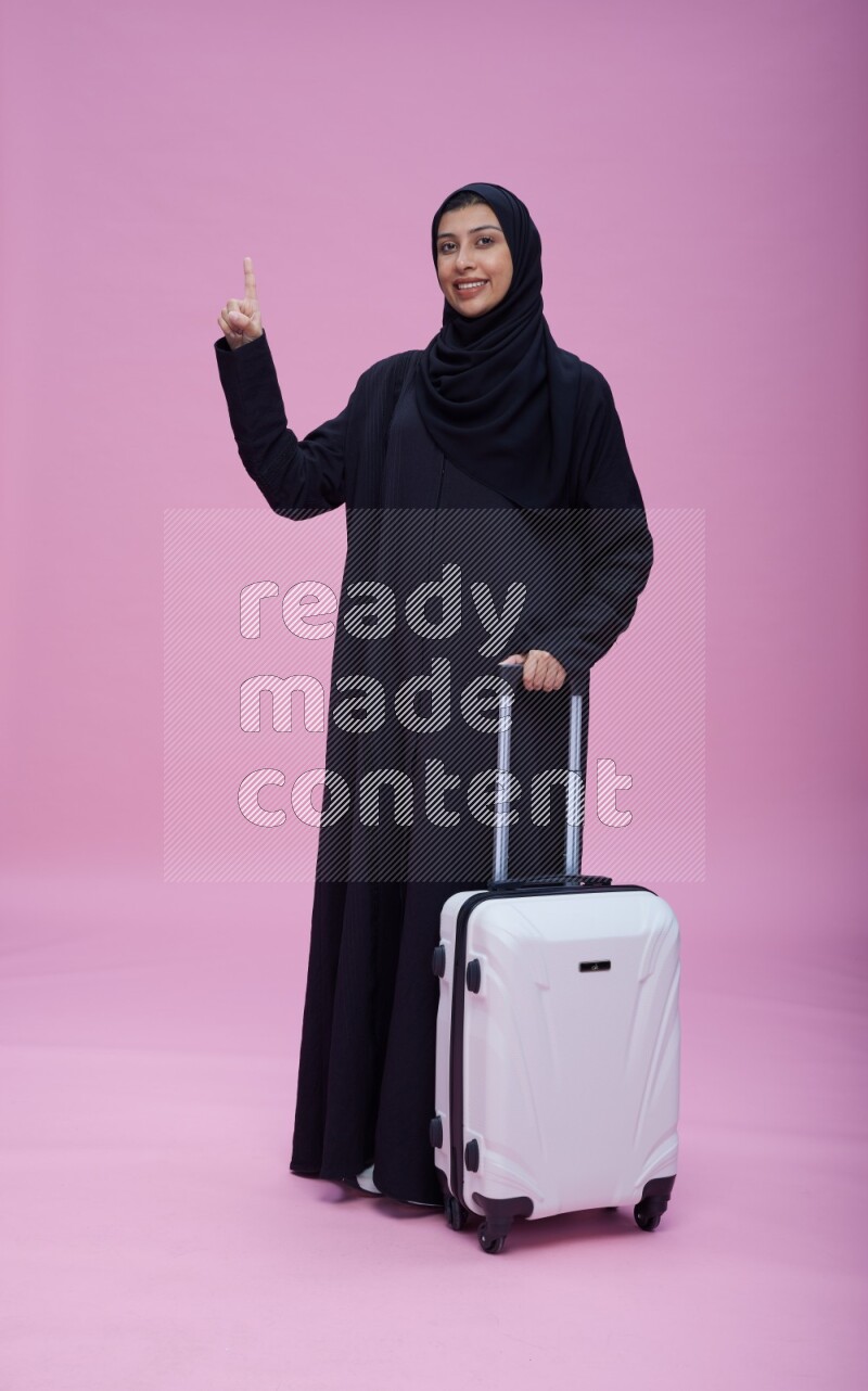 Saudi woman wearing Abaya standing holding bag on pink background