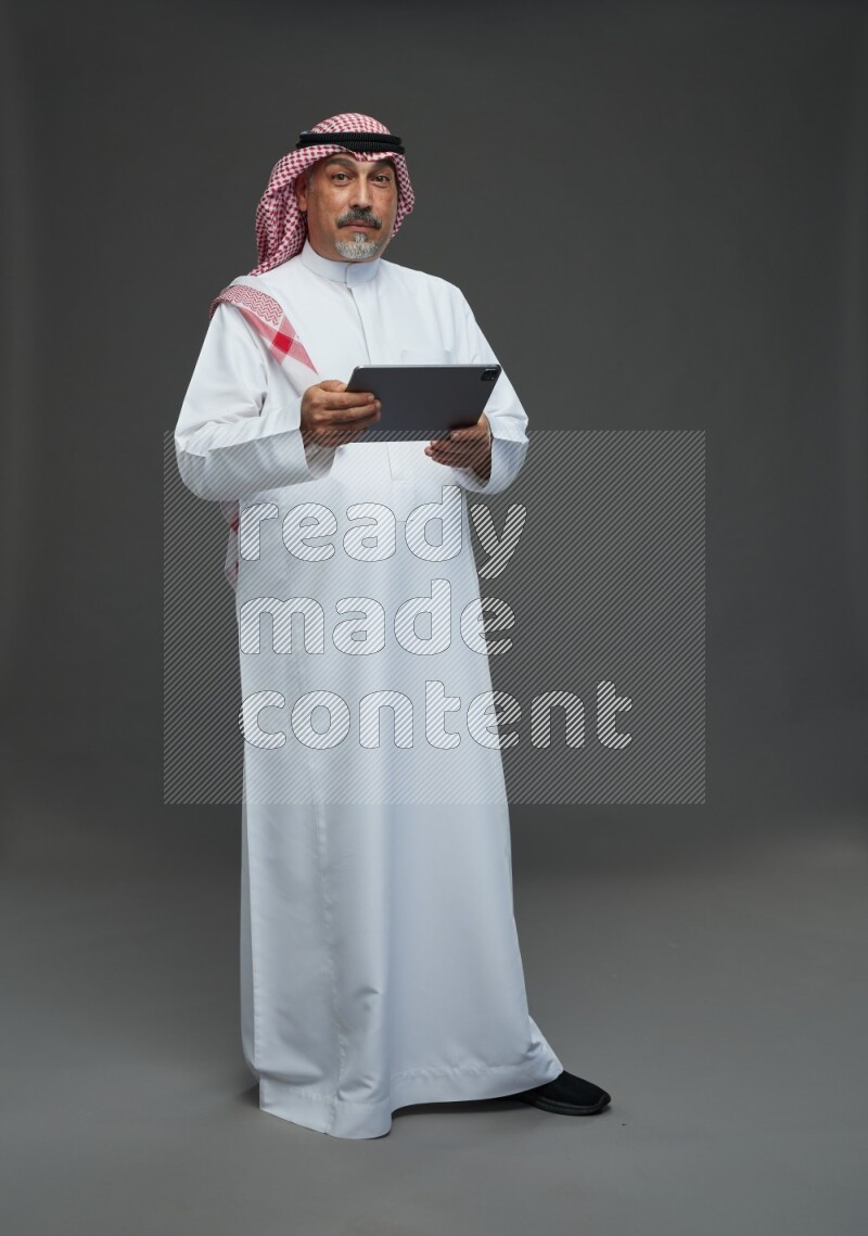 Saudi man with shomag Standing working on tablet on gray background