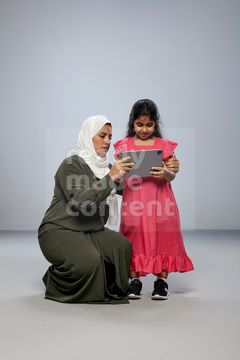 A girl holding an Ipad with her mother on gray background