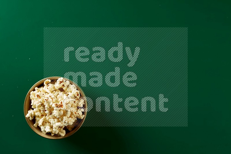 An off white ceramic bowl full of popcorn on a green background in a top view shot
