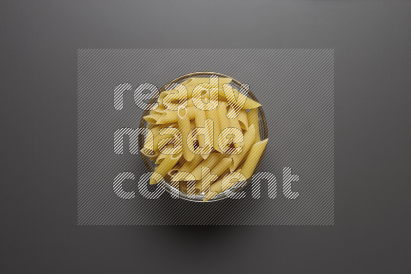 Penne pasta in a glass bowl on grey background