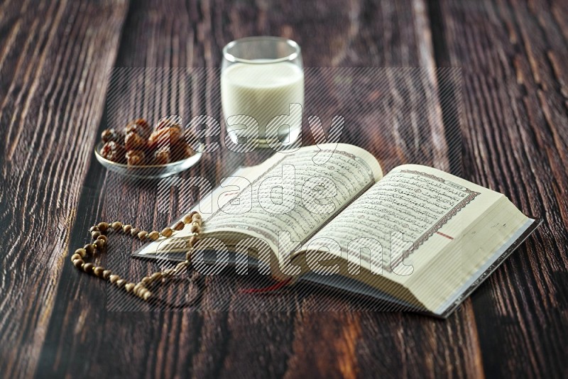 Quran with dates, prayer beads and different drinks all placed on wooden background