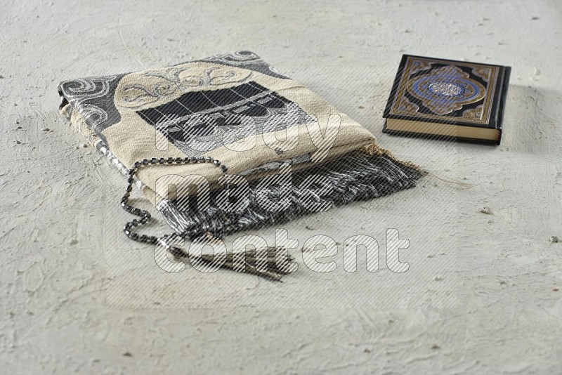 A prayer rug with different elements such as quran and prayer beads on white textured background