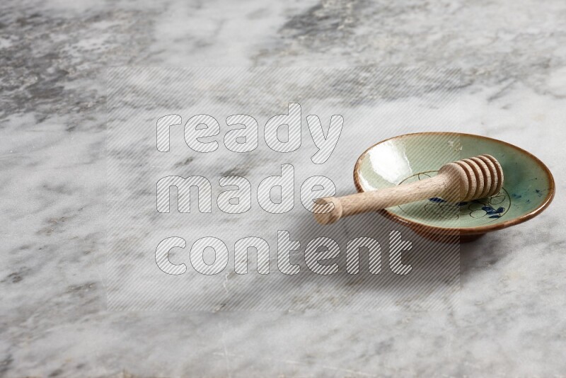 Decorative pottery plate with wooden honey dipper in it on grey marble background