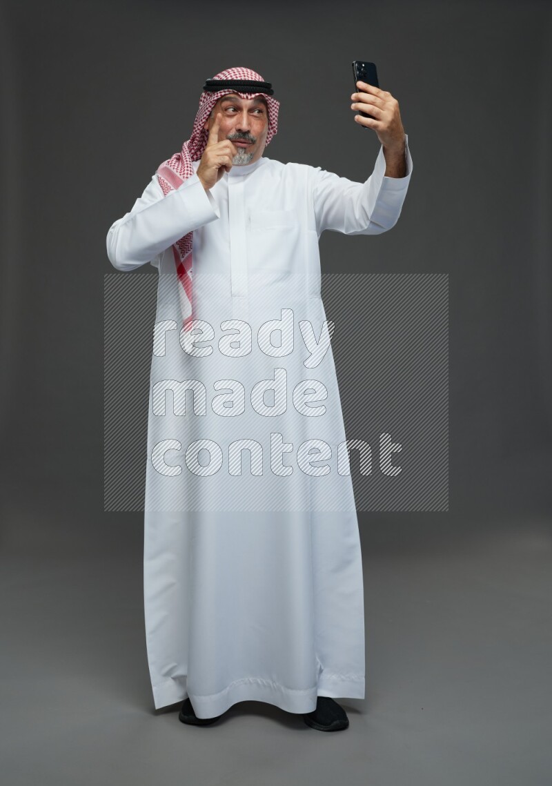 Saudi man with shomag Standing taking selfie on gray background