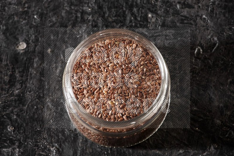 A glass jar full of flaxseeds on a textured black flooring