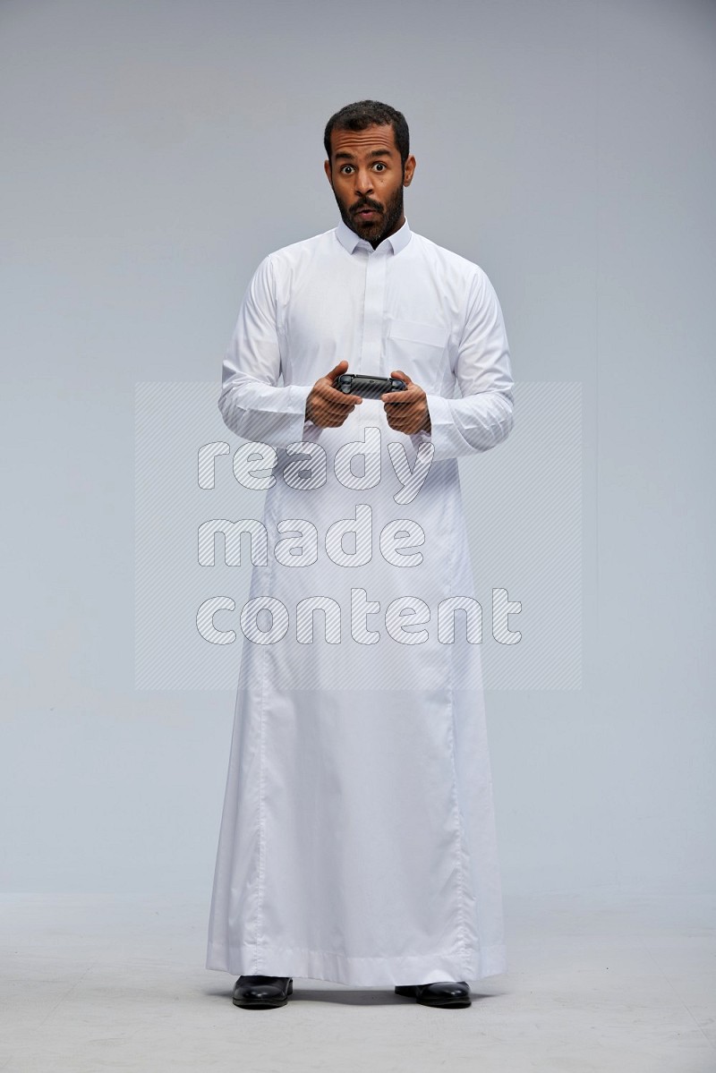 Saudi man Wearing thob standing holding joystick on Gray background