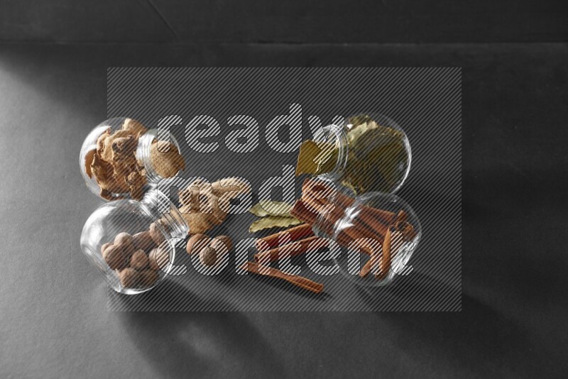 أوراق الغار وزنجبيل مجفف وقرفة وجوزة الطيب في أوعية زجاجية علي خلفية سوداء