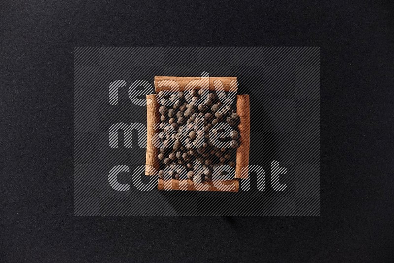 A single square of cinnamon sticks full of allspice on black flooring