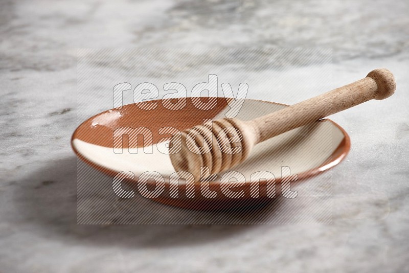 Multicolored Pottery Plate with wooden honey handle in it, on grey marble flooring, 15 degree angle