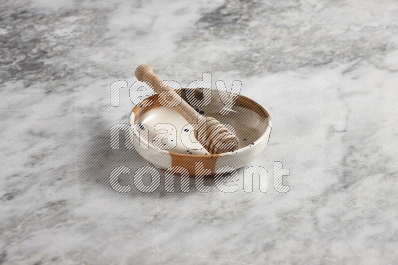 Multicolored pottery bowl with wooden honey dipper in it on grey marble background