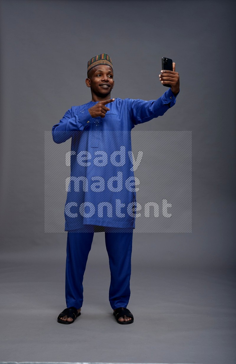 Man wearing Nigerian outfit standing taking selfie on gray background