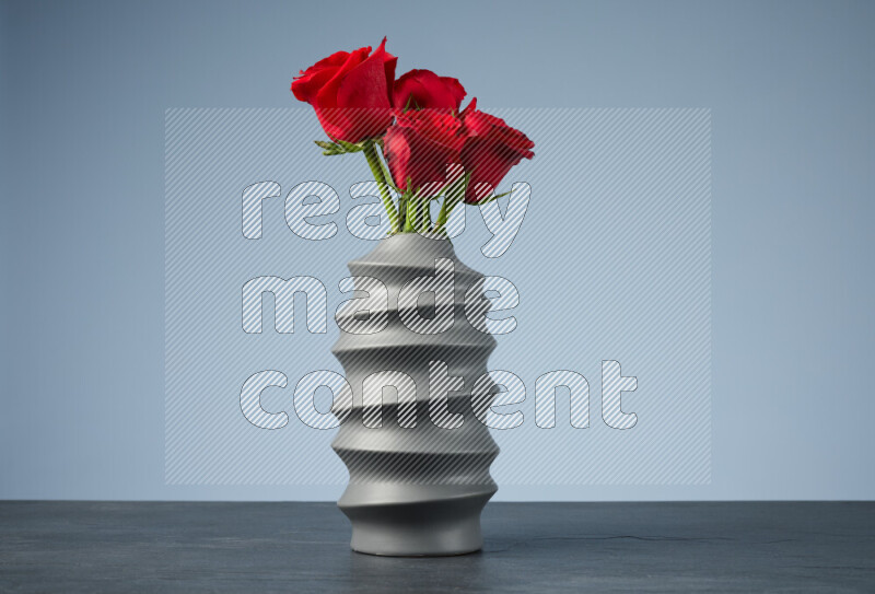 An arrangement of vivid red roses in a grey spiral vase on black marble background