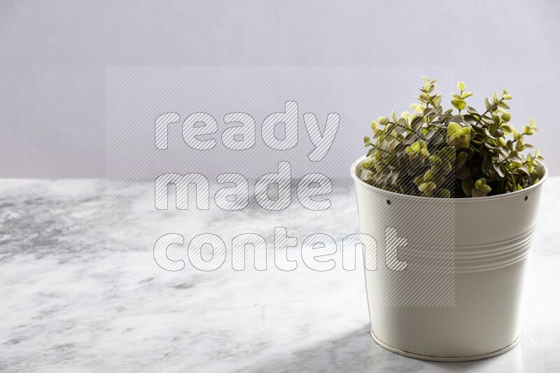 Green artificial plant in white pot on light grey marble background