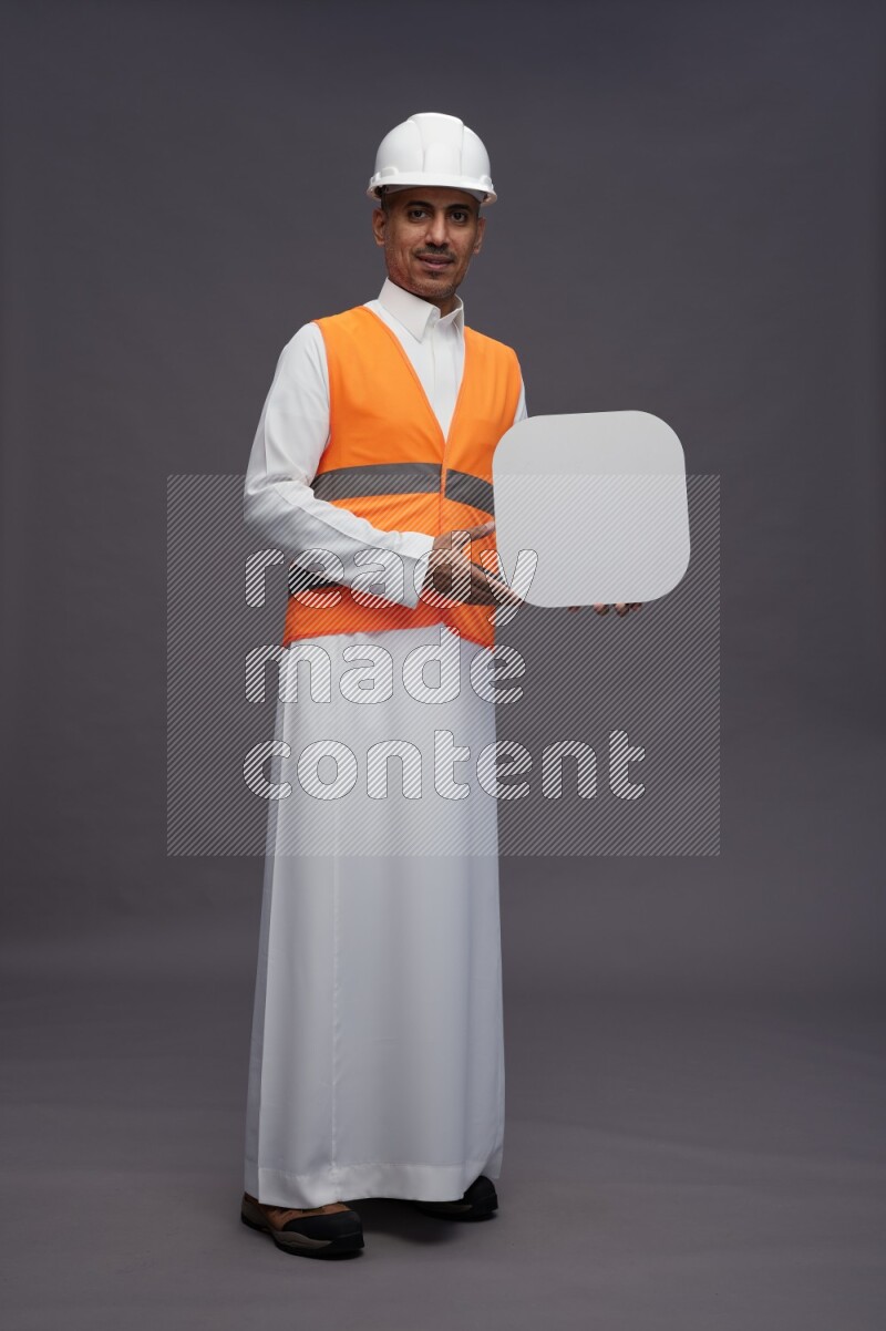Saudi man wearing thob with engineer vest standing holding social media sign on gray background
