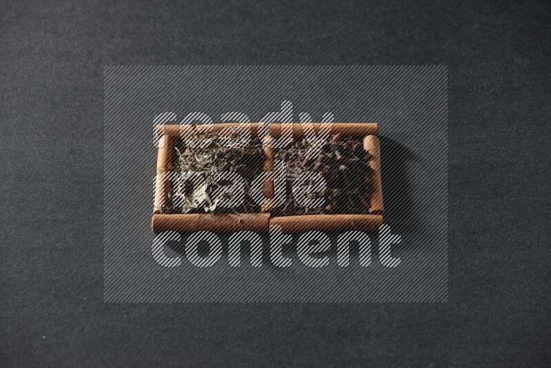 مربعان من أعواد القرفة ممتلئان بالقرنفل والريحان المجفف علي خلفية سوداء