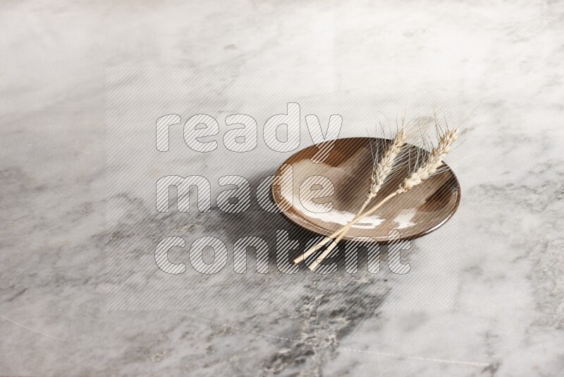 Wheat stalks on multicolored pottery plate on grey marble background