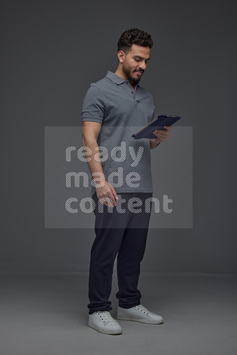 A man wearing casual standing and using his tablet and making multi hand gestures different angles eye level on a gray background