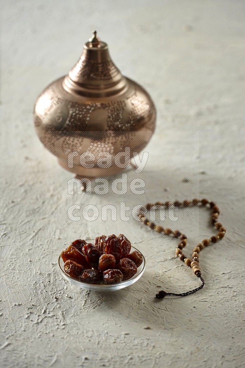 A golden lantern with drinks, dates, nuts, prayer beads and quran on textured white background